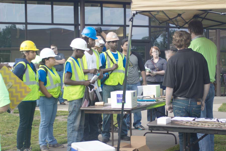 Workers in hard hats and bright vests standing at a table where someone is speaking to them